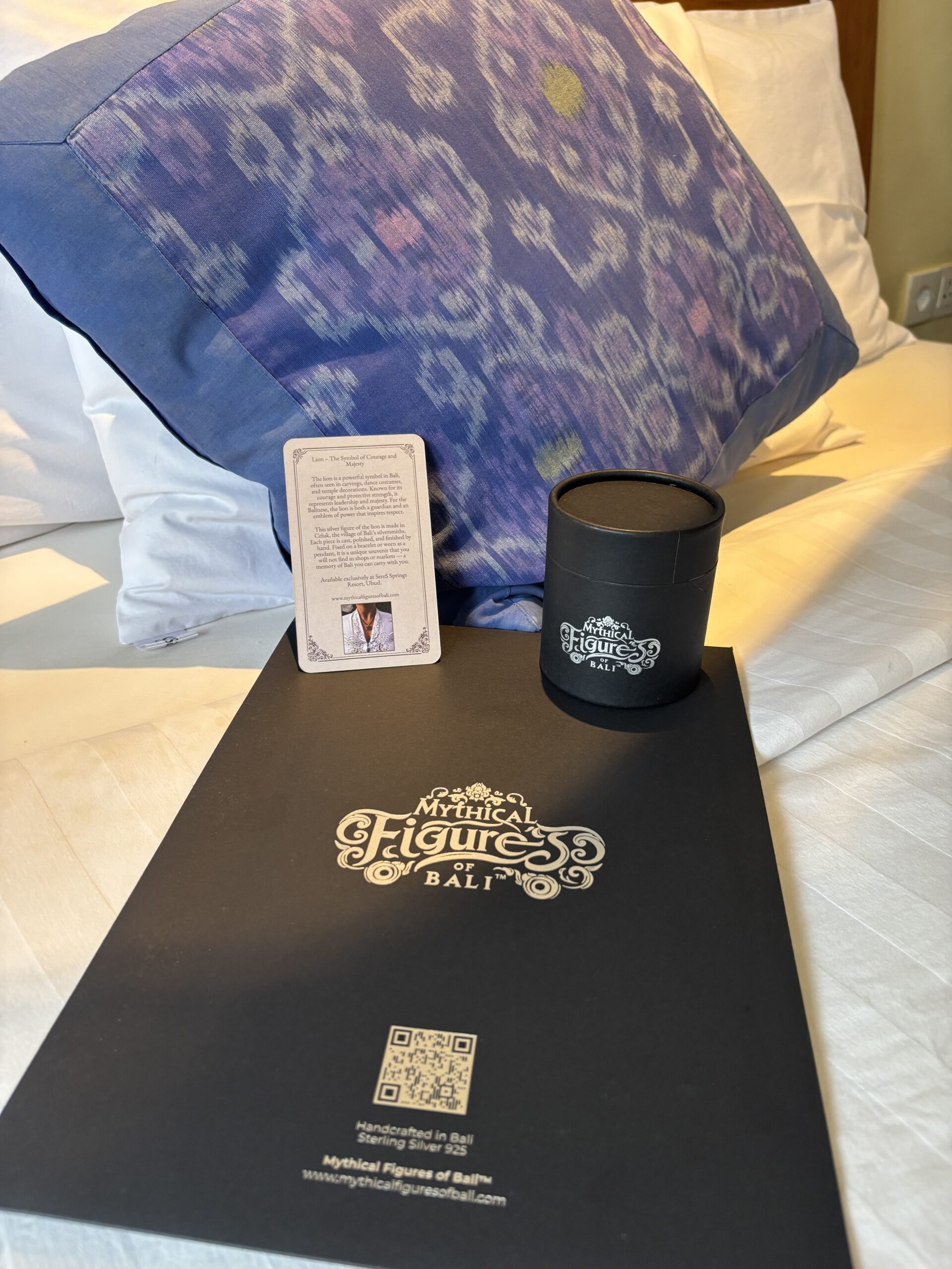 The delegate experience — black cylinder, mythology card, and envelope presented on a bed with ikat cushion